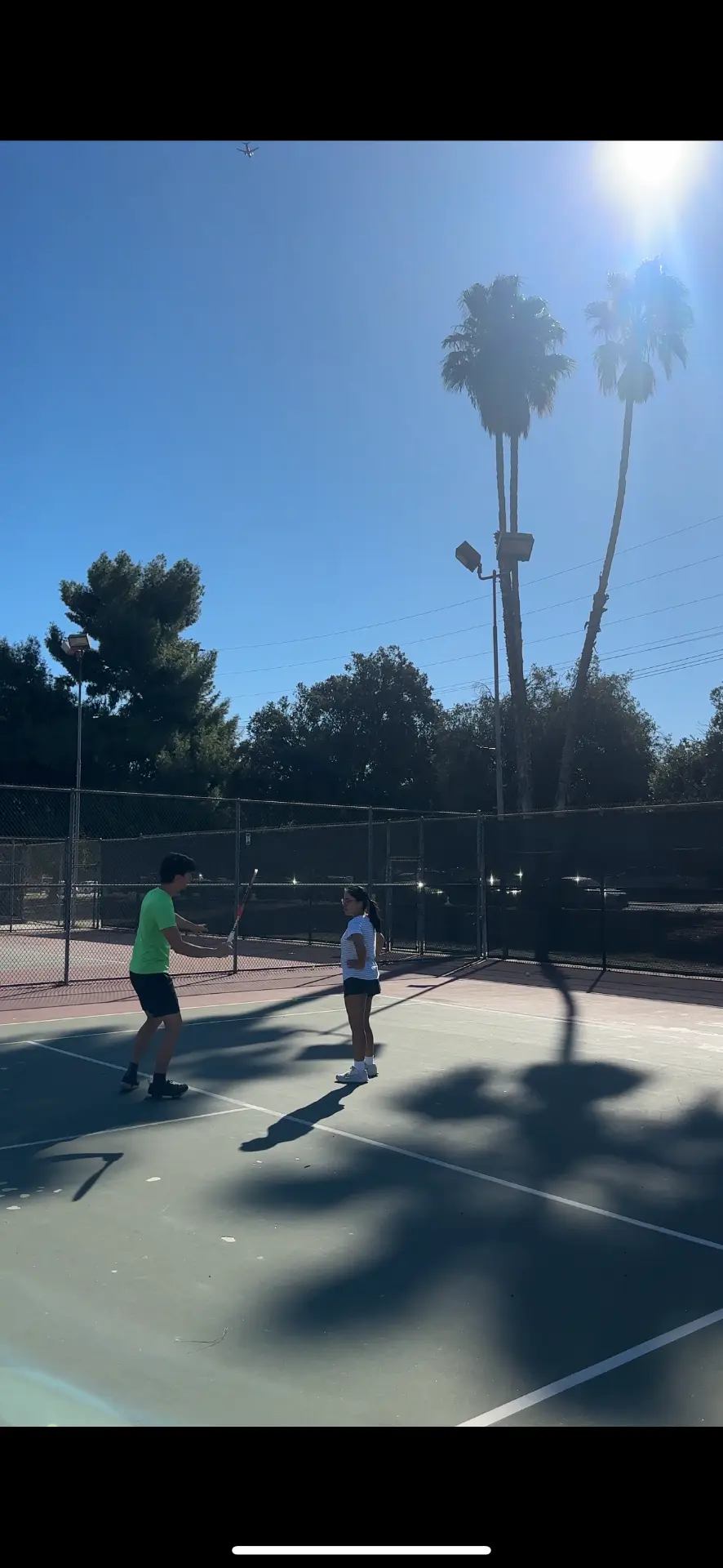 Poom coaching a player during a lesson on an outdoor tennis court